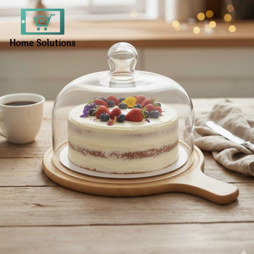 Decorative cake with fruit on a wooden board under a glass dome, set on a table.