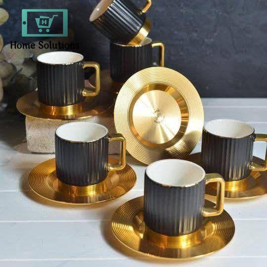 Set of black and gold ceramic cups and saucers on a white surface with a dark background.