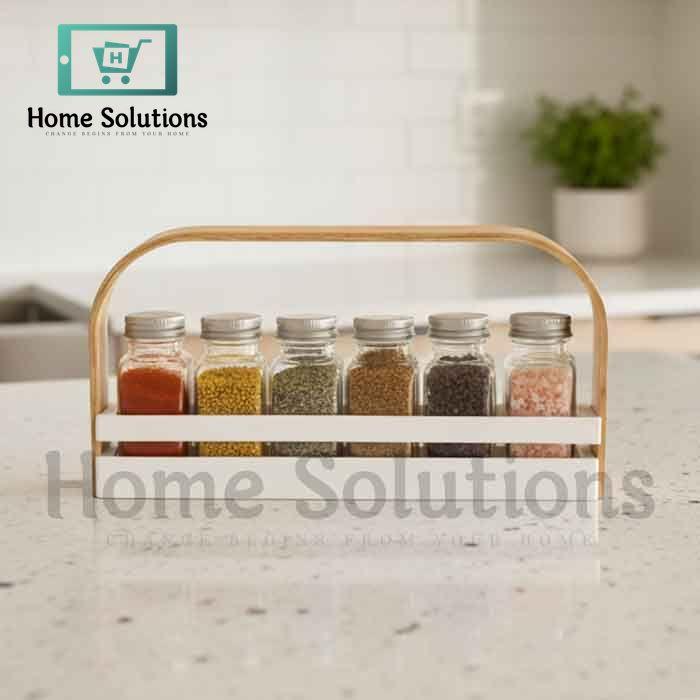 White wooden spice jar caddy with a light brown handle holding six clear glass jars with silver metal lids, organized for a modern Pakistani kitchen