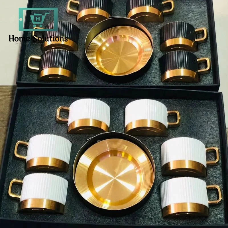 Set of gold and white cups with metal rims and metal saucers in a black box.