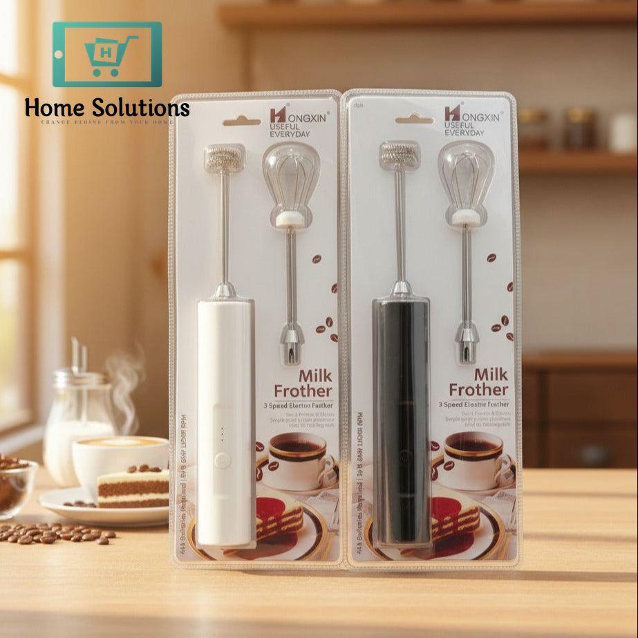 Two milk frothers in packaging on a kitchen counter with coffee and cake in the background.