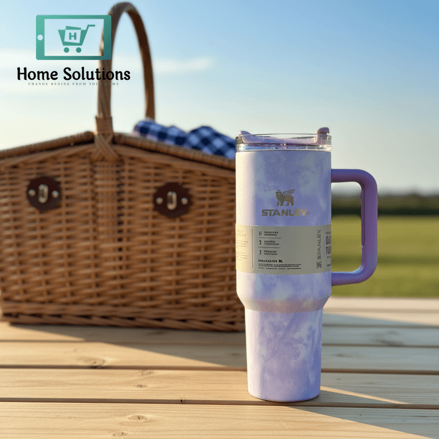 Purple insulated tumbler on a wooden table with a picnic basket and blanket in the background.
