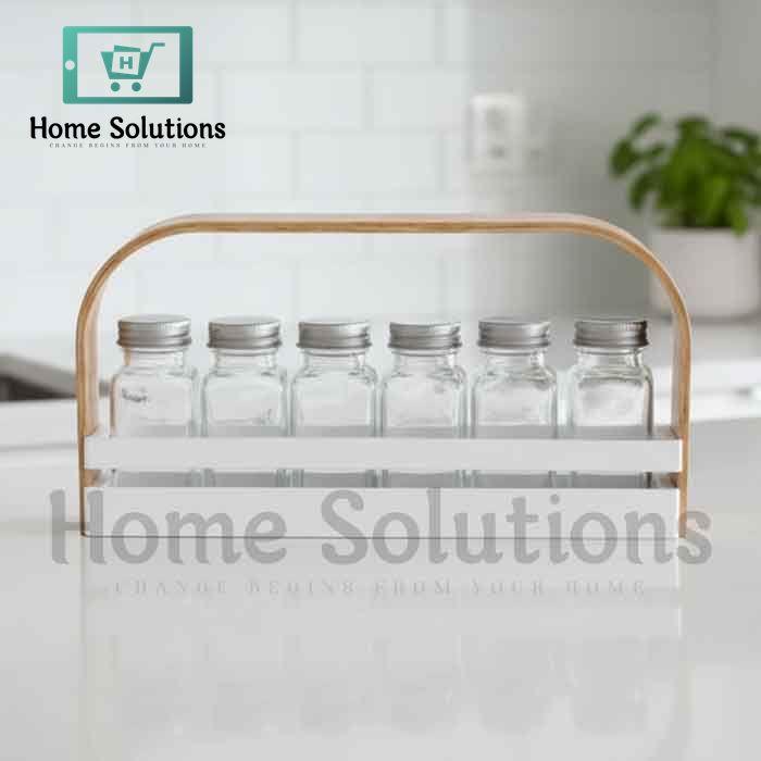 White wooden spice jar caddy with a light brown handle holding six clear glass jars with silver metal lids, organized for a modern Pakistani kitchen