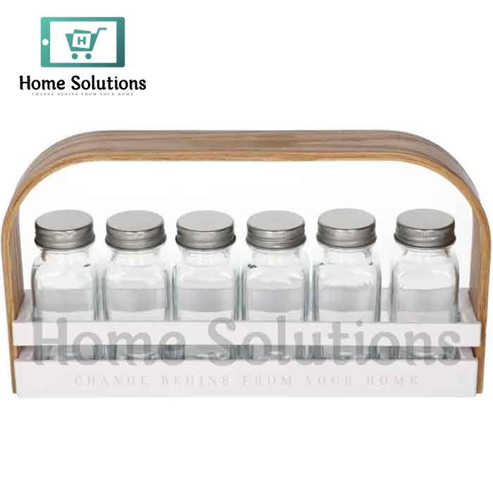 White wooden spice jar caddy with a light brown handle holding six clear glass jars with silver metal lids, organized for a modern Pakistani kitchen