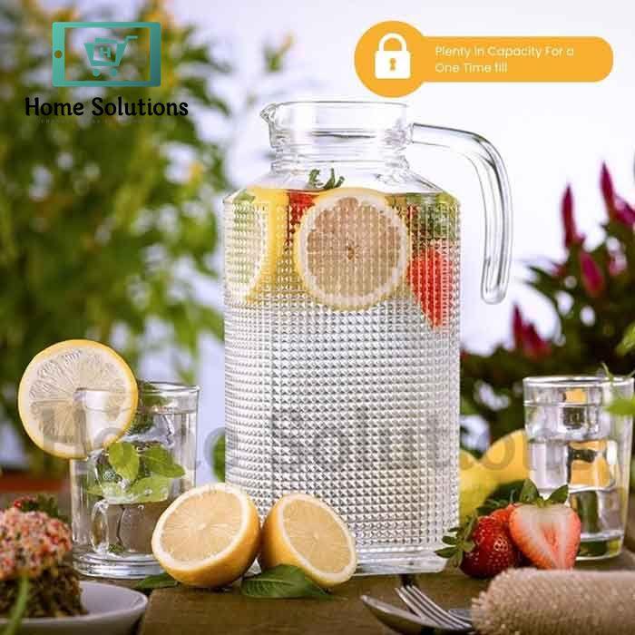 Clear glass pitcher with lemon and strawberry slices on a table outdoors.