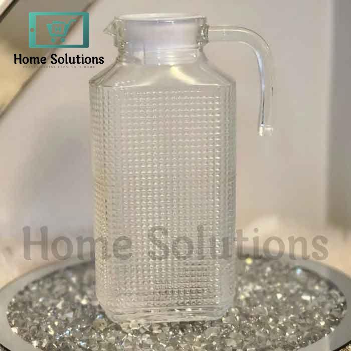 Clear glass pitcher with textured surface on a reflective surface, branded 'Home Solutions'.