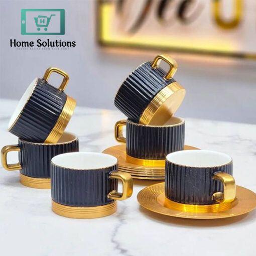 Set of black and gold ceramic coffee cups and saucers on a marble surface