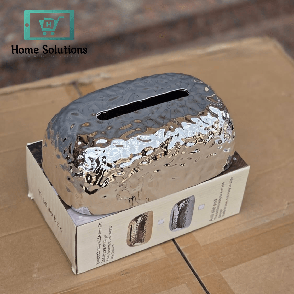 Silver textured hammered chick tissue box on a cardboard box with a blurred background