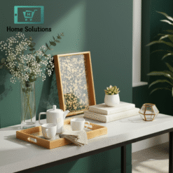 Decorative tray set with books, teacups, and a plant against a green wall.