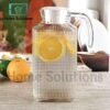 Clear glass pitcher with lemon slices on a wooden surface, branded 'Home Solutions'.