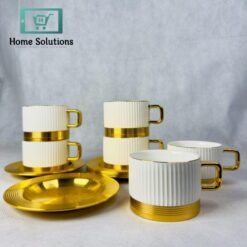 Set of 6 elegant ribbed ceramic coffee and tea cups with gold metal bases and matching gold metal saucers, stacked on a marble surface with blurred golden background