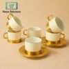 Set of white cups with gold metal rims and handles with metal on a beige background