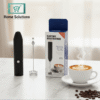 Electric milk frother with packaging, a cup of coffee, and coffee beans on a marble surface.