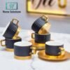 Set of black and gold ceramic coffee cups and saucers on a marble surface